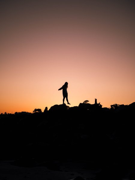 silhouetted person walking from rock to rock